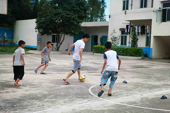 廣東醫科大學“微塵·心”公益團隊在廣東省廉江市塘蓬鎮同留小學支教，志願者帶男同學踢足球。