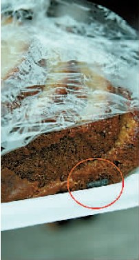 解开保鲜膜，蛋糕一角有颗耗子屎（红圈处）。