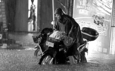 10日晚,广西柳州,一名市民在雨中推车通过积水路段。 图/东方IC