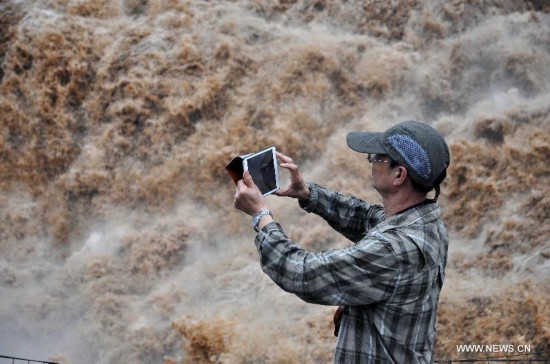 A tourist takes photos of the Hukou Waterfall of the Yellow River, north China's Shanxi Province, July 9, 2014. (Xinhua/Fan Minda) 