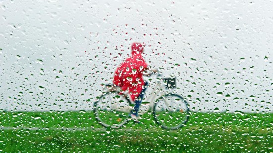 A woman in a red raincoat is pictured through a window covered with raindrops as she rides her bike near Reichling, southern Germany, Wednesday, July 9, 2014. 