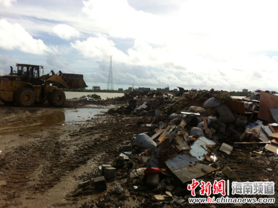 新埠岛东坡村南渡江沿岸上,垃圾成堆,一推土机正向江边推入垃圾。