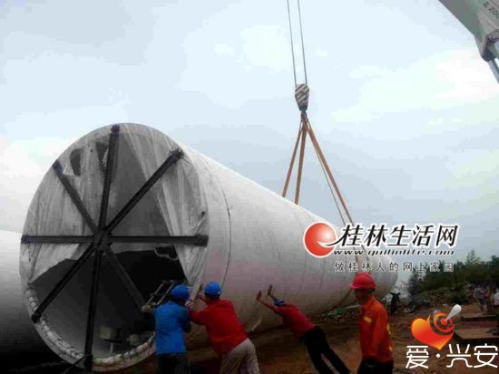 在西岭风电场9号坑位附近，重型吊机将塔筒从运输车上卸下。