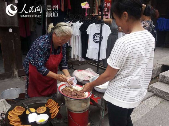 圖為游客向徐業梅買當地小吃。王欽攝