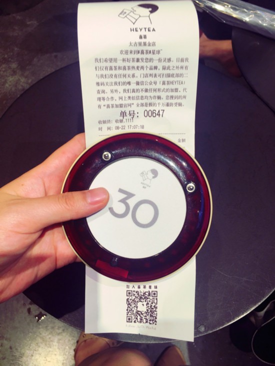 终于排到了喜茶店内，记者买了两杯店内推荐的喜茶品种“金凤茶王”和“四季春”。又拿到一个号码牌，意味着还要等一段时间才能拿到喜茶。