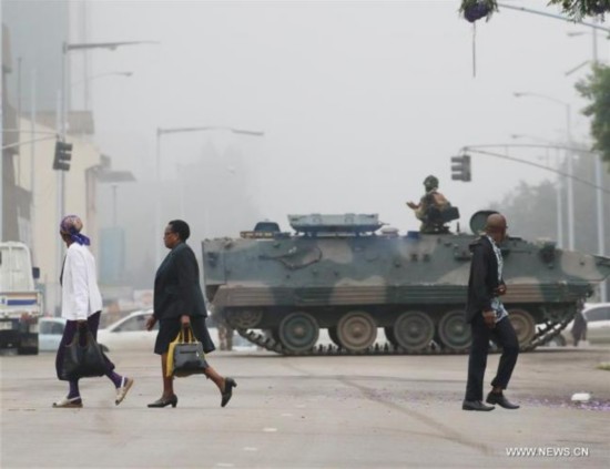 People walk past an armored vehicle on a street in Harare, capital of Zimbabwe, Nov. 15, 2017. Armored carriers cordoned off Zimbabwe's Presidential seat of power and Parliament Building in the capital while helicopters circled the city center on a drizzly morning, after the military announced it had taken over control of all government institutions. [Photo: Xinhua/Philimon Bulawayo]