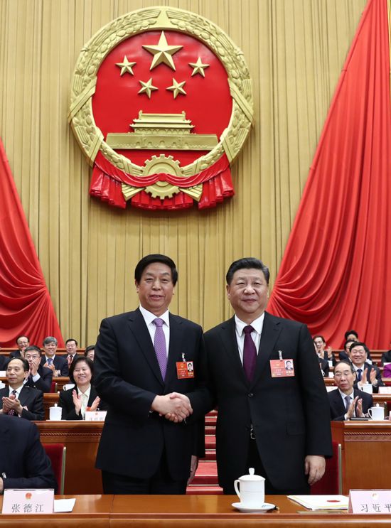习近平在主席台上同新当选的全国人大常委会委员长栗战书握手.