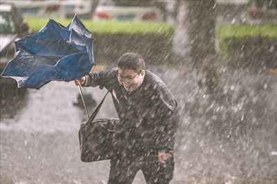一名上班族在雨中奔跑,伞被狂风吹翻.