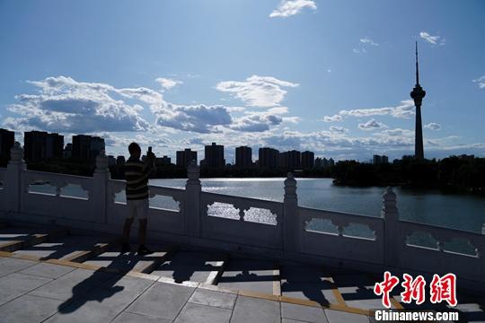 北京の玉淵潭公園で、白い雲が浮かぶ青空の写真を撮る人（撮影・張興竜）。