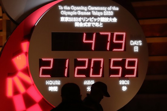 3月30日,行人经过日本东京站前显示东京奥运会开幕式倒计时的电子钟,电子钟已根据新宣布的开幕时间进行调整。