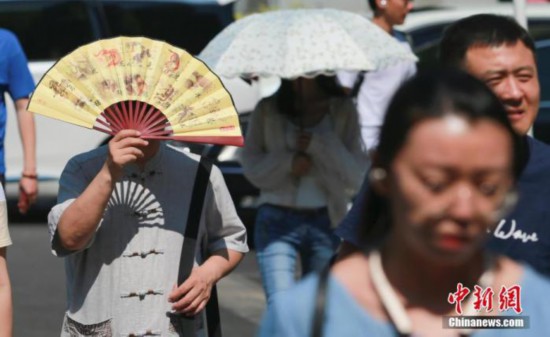 北京の街を日差しを遮りながら歩く人々（資料写真、撮影・賈天勇）。