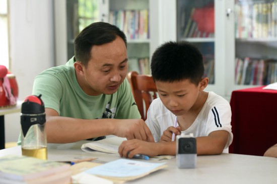 7月22日，在樅陽縣橫埠鎮方正小學安置點“愛心教室”裡，方正小學老師操磊（左）指導小朋友寫暑假作業。