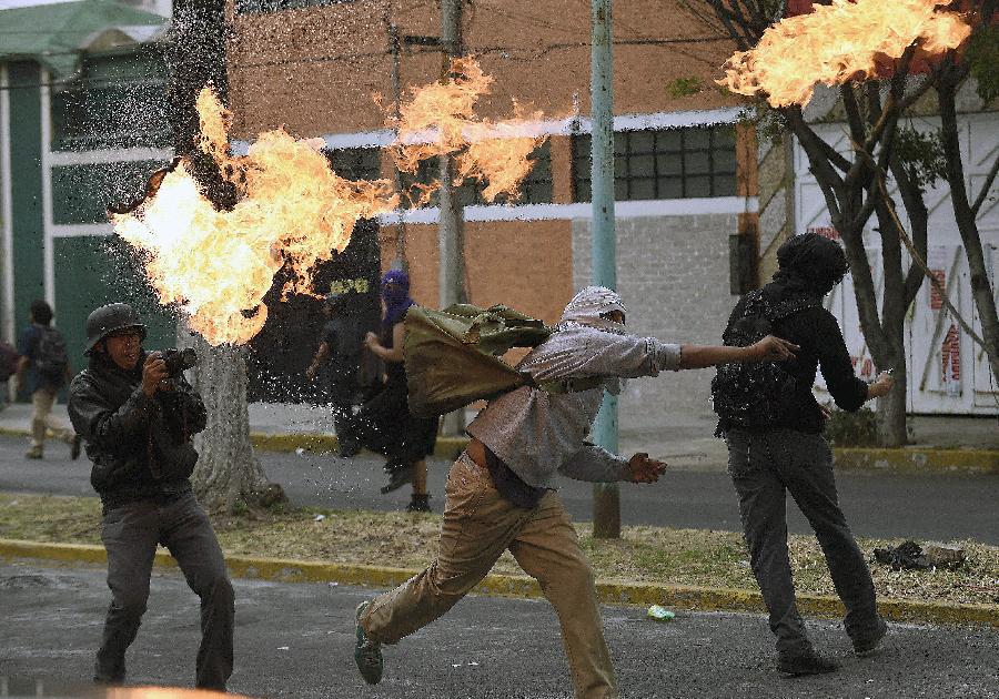 A masked demonstrator throws a petrol bomb towards riot police during a protest over the 43 missing Ayotzinapa students in Mexico City November 20, 2014.