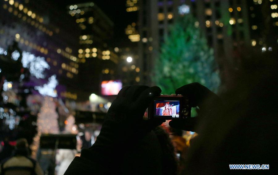 A visitor takes photos of American singer Mariah Carey's performance in front of the Christmas tree during the 82nd Christmas Tree Lighting Ceremony in Rockefeller Center in New York, the United States, Dec. 3, 2014.