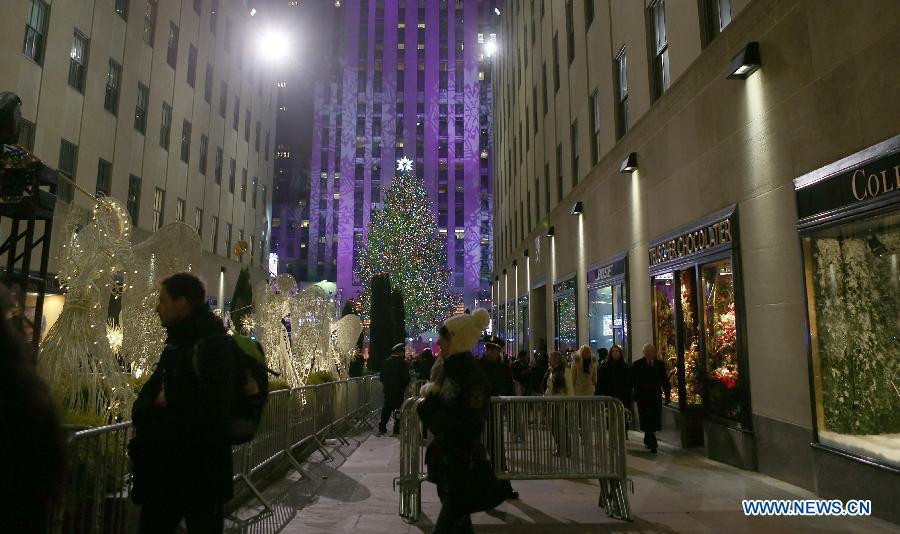 People walk past by the Christmas tree with all the lights lit up after the 82nd Christmas Tree Lighting Ceremony in Rockefeller Center in New York, the United States, Dec. 3, 2014.