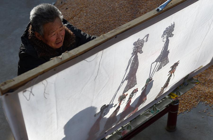 Cao Zhiqin, a shadow play puppeteer, manipulates leather puppets during a performance in Zhenhu Township of Xiji County, Guyuan, northwest China's Ningxia Hui Autonomous Region, Jan. 12, 2014. The Chinese shadow play is performed by manipulating flat leather puppets against a lit-up translucent screen. The art form was registered in the Representative List of the Intangible Cultural Heritage of Humanity by the UNESCO in 2011. Cao Zhiqin, who is 67, started learning shadow puppetry when he was a child. As head of a local puppetry troupe, Cao has worked hard to promote shadow puppetry, hoping that people can still enjoy the fun of this folk art. (Xinhua/Li Ran)
