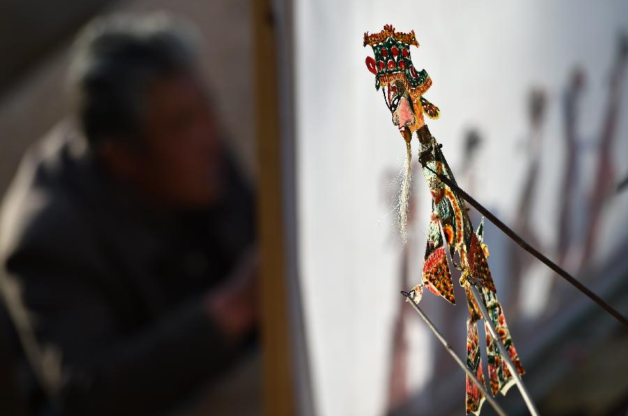 Cao Zhiqin, a shadow play puppeteer, manipulates leather puppets during a performance in Zhenhu Township of Xiji County, Guyuan, northwest China's Ningxia Hui Autonomous Region, Jan. 12, 2014. The Chinese shadow play is performed by manipulating flat leather puppets against a lit-up translucent screen. The art form was registered in the Representative List of the Intangible Cultural Heritage of Humanity by the UNESCO in 2011. Cao Zhiqin, who is 67, started learning shadow puppetry when he was a child. As head of a local puppetry troupe, Cao has worked hard to promote shadow puppetry, hoping that people can still enjoy the fun of this folk art. (Xinhua/Li Ran)