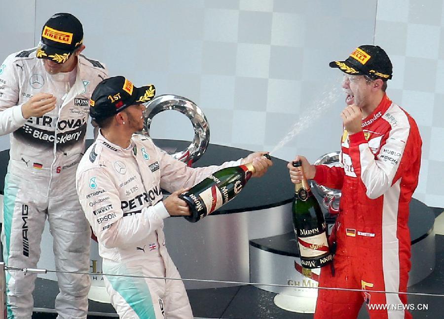 Mercedes AMG driver Lewis Hamilton (C) of Britain sprays champagne on Ferrari driver Sebastian Vettel (R) of Germany after winning the Chinese Formula One Grand Prix at Shanghai International Circuit in Shanghai, China, April 12, 2015. 