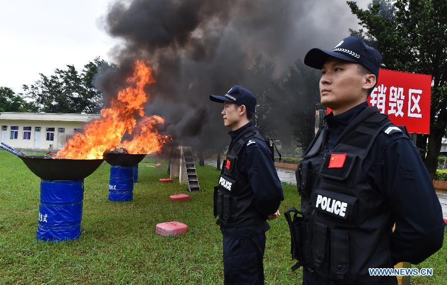 Police officers stand guard beside burning drugs.