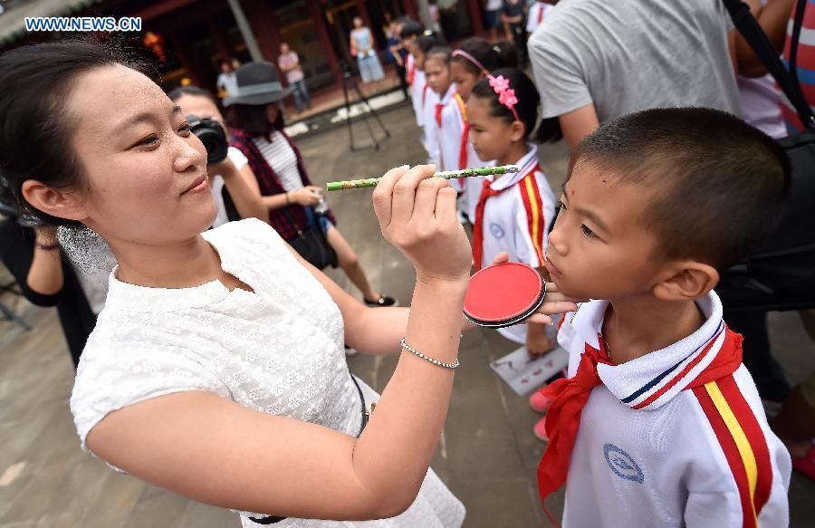 A teacher draws red dots, a traditional gesture symbolizing enlightening, for students at the Confucius classroom in the Confucius temple of Wenchang, south China's Hainan Province, July 10, 2015.