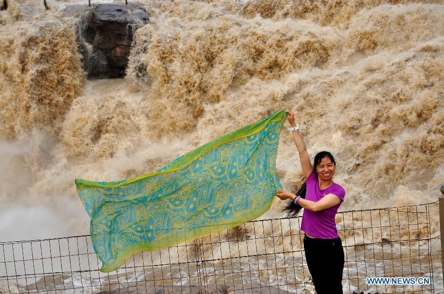 A tourist poses for photos at Hukou Waterfall on the Yellow River in Linfen, north China's Shanxi Province, July 10, 2015. 