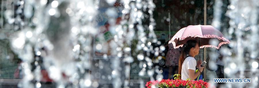 A woman walks past a fountain with an umbrella to shield from the scorching sun in Yinchuan, capital of northwest China's Ningxia Hui Autonomous Region, July 24, 2015. 