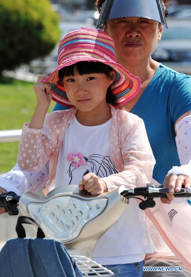 A woman, carring her child, rides on a street in Yinchuan, capital of northwest China's Ningxia Hui Autonomous Region, July 24, 2015. 