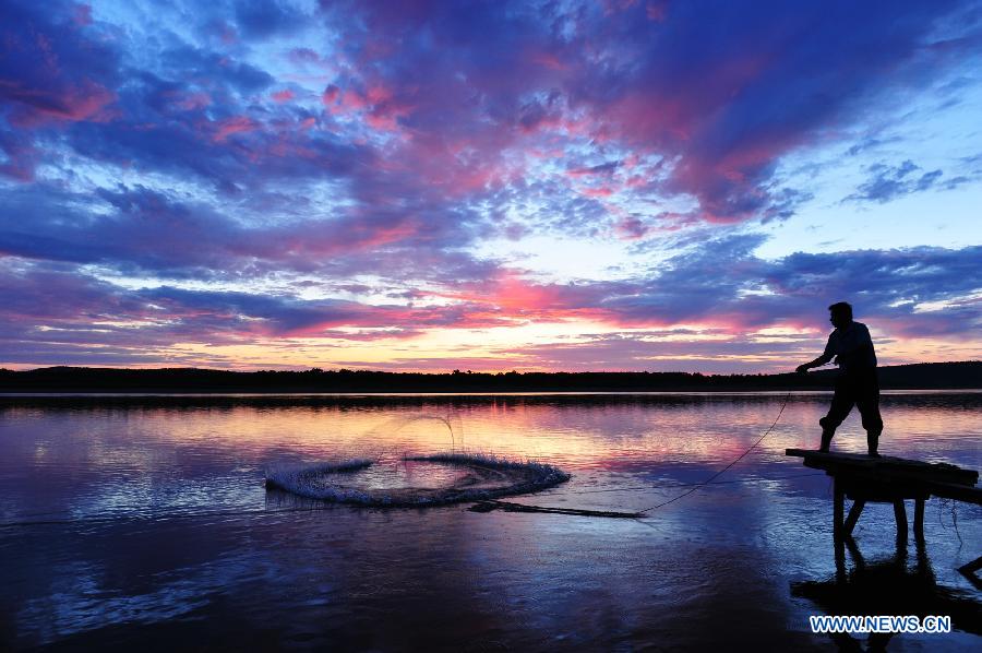 A fisherman catches fish at sunrise on Huma section of Heilongjiang River in northeast China's Heilongjiang Province, July 19, 2015.