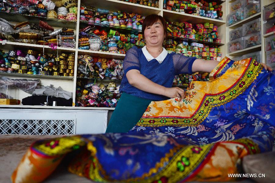 A woman presents traditional handmade clothes of Yugu ethnic group in a store in Sunan Yugu Autonomous County of northwest China's Gansu Province, July 30, 2015. Various studios were set by local government this year to preserve and promote Yugu ethnic group's intangible cultural heritages, such as ballads, embroidery and wedding customs. (Xinhua/Chen Bin) 