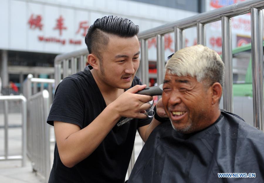 Barber Hong Tao gives a homeless man free haircuts at the railway station in Zhengzhou, capital of central China's Henan Province, Aug. 4, 2015.