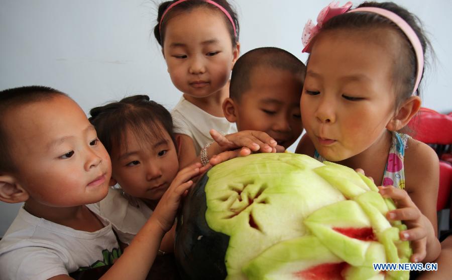 Children watch a watermelon carved with Chinese characters 'beginning of autumn'in Liujiayao Village of Zhangjiakou City, north China's Hebei Province, Aug. 7, 2015.