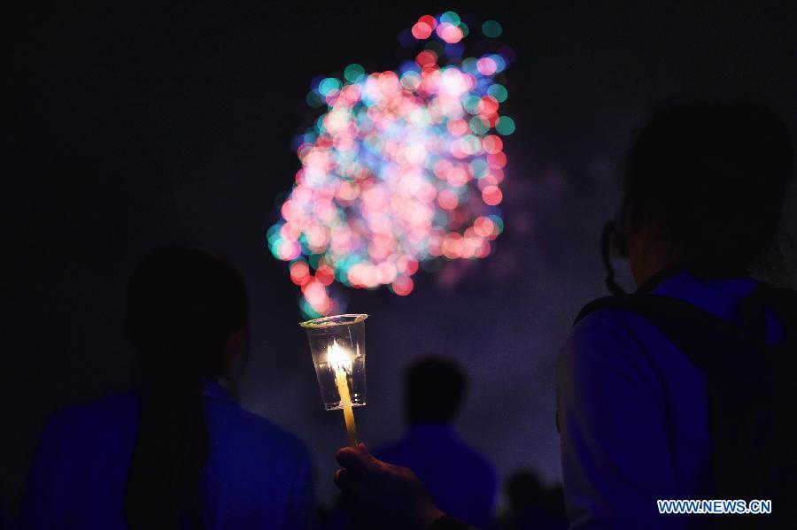 A participator holds a candle while watching the fireworks during an event celebrating Queen Sirikit's 83rd birthday at the Sanam Luang square in Bangkok, Thailand, on Aug. 12, 2015. 