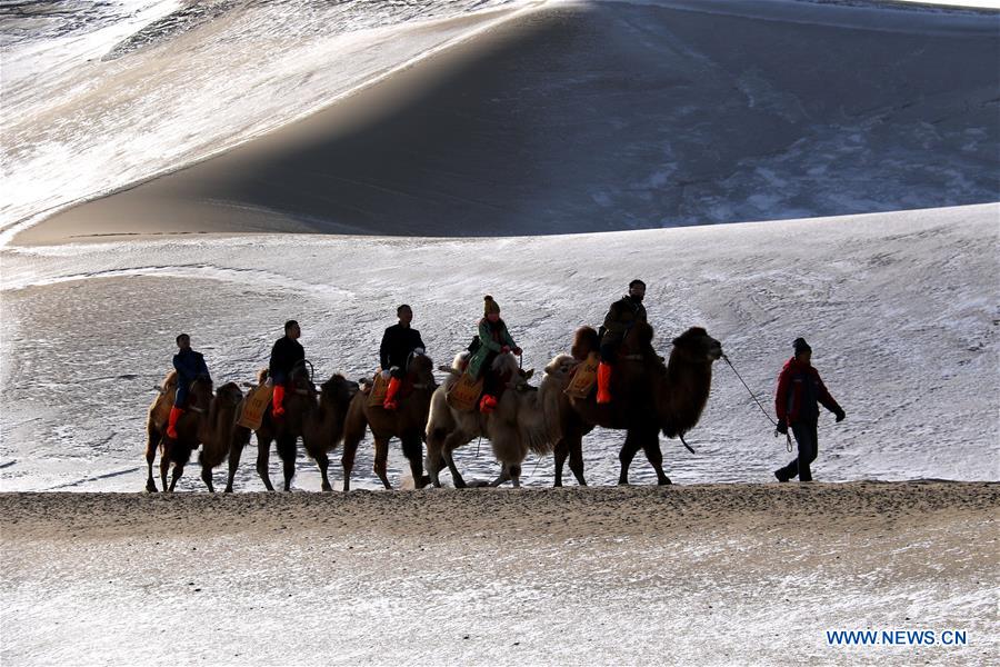 People riding camels visit the Crescent Lake scenery spot in Mingsha Mountain of Dunhuang City, northwest China's Gansu Province, Dec. 13, 2015.