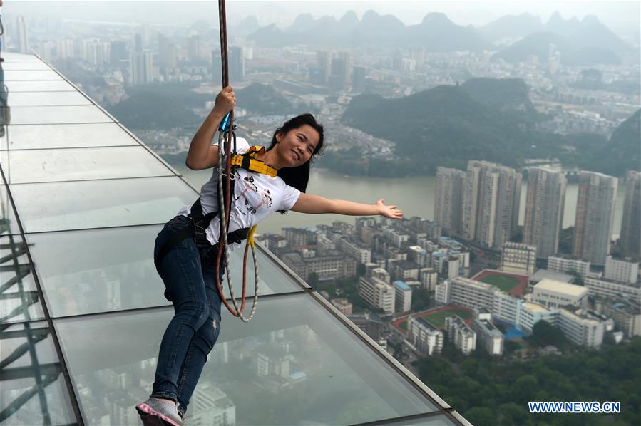 A tourist fastened by safty belt experiences sightseeing in the air on the Yunding glass-made plank road on a skyscraper in Liuzhou, south China's Guangxi Zhuang Autonomous Region, May 5, 2016.