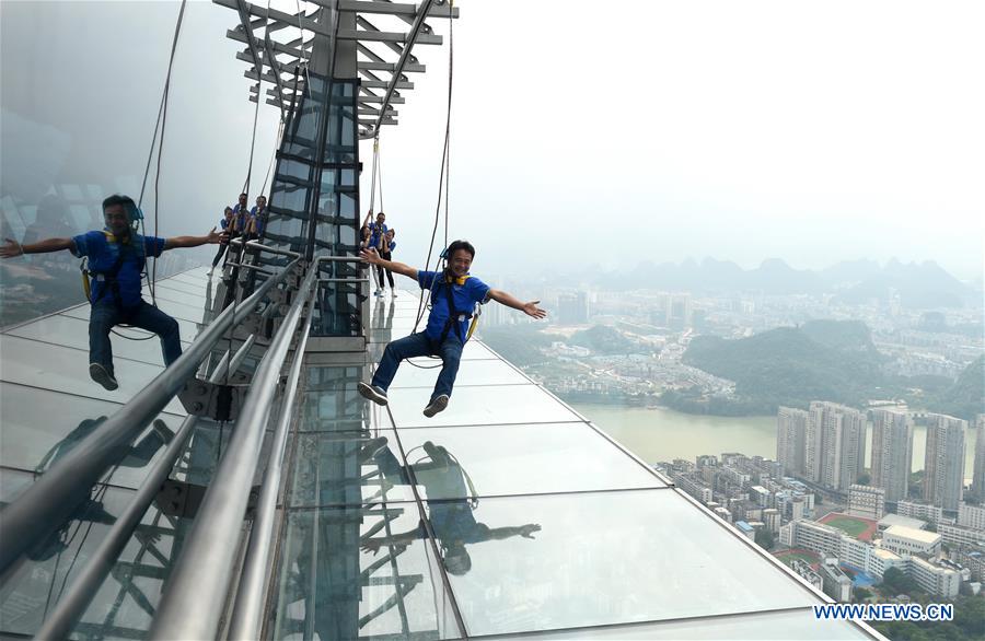 A tourist fastened by safty belt experiences sightseeing in the air on the Yunding glass-made plank road on a skyscraper in Liuzhou, south China's Guangxi Zhuang Autonomous Region, May 5, 2016. 