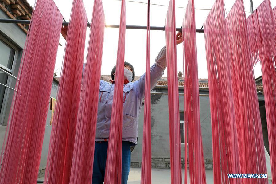 A staff member airs colored noodles at a workshop in Binzhou, east China\'s Shandong Province, Jan. 29, 2019. These noodles are naturally colored using vegetables or fruits such as carrot, spinach and dragon fruit. (Xinhua/Zhang Chunfeng)