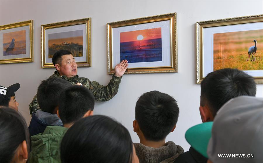 Shuanglong, a man of Mongolian ethnic group, leads primary students to visit his photo exhibition in New Barag Right Banner of the Hulun Buir City, north China\'s Inner Mongolia Autonomous Region, April 13, 2019. Shuanglong, a volunteer born in the 1980s, has been dedicated to protecting wildlife inhabiting along the Hulun Lake over the past ten years. Over 40 endangered animals have been saved through his efforts. Shuanglong has organized various activities including photo exhibitions and lectures, as a way to raise awareness of wildlife protection among the public. Affected by Shuanglong, some volunteers also joined him to protect wildlife along the Hulun Lake. (Xinhua/Peng Yuan)