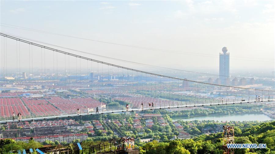 Aerial photo taken on May 4, 2019 shows tourists walking on a glass bridge at the Huaxi World Adventure Park in Huaxi Village of Jiangyin City, east China\'s Jiangsu Province. The 518-meter-long glass bridge hangs more than 100 meters above ground level at the park. It is made of panes of 35-mm-thick glass. Each glass can hold a maximum weight of 4.7 tonnes. Around 2,600 people can cross the bridge at a time. (Xinhua/Xu Congjun)