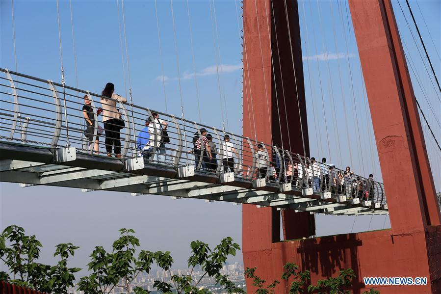 Tourists walk on a glass bridge at the Huaxi World Adventure Park in Huaxi Village of Jiangyin City, east China\'s Jiangsu Province, May 4, 2019. The 518-meter-long glass bridge hangs more than 100 meters above ground level at the park. It is made of panes of 35-mm-thick glass. Each glass can hold a maximum weight of 4.7 tonnes. Around 2,600 people can cross the bridge at a time. (Xinhua/Xu Congjun)